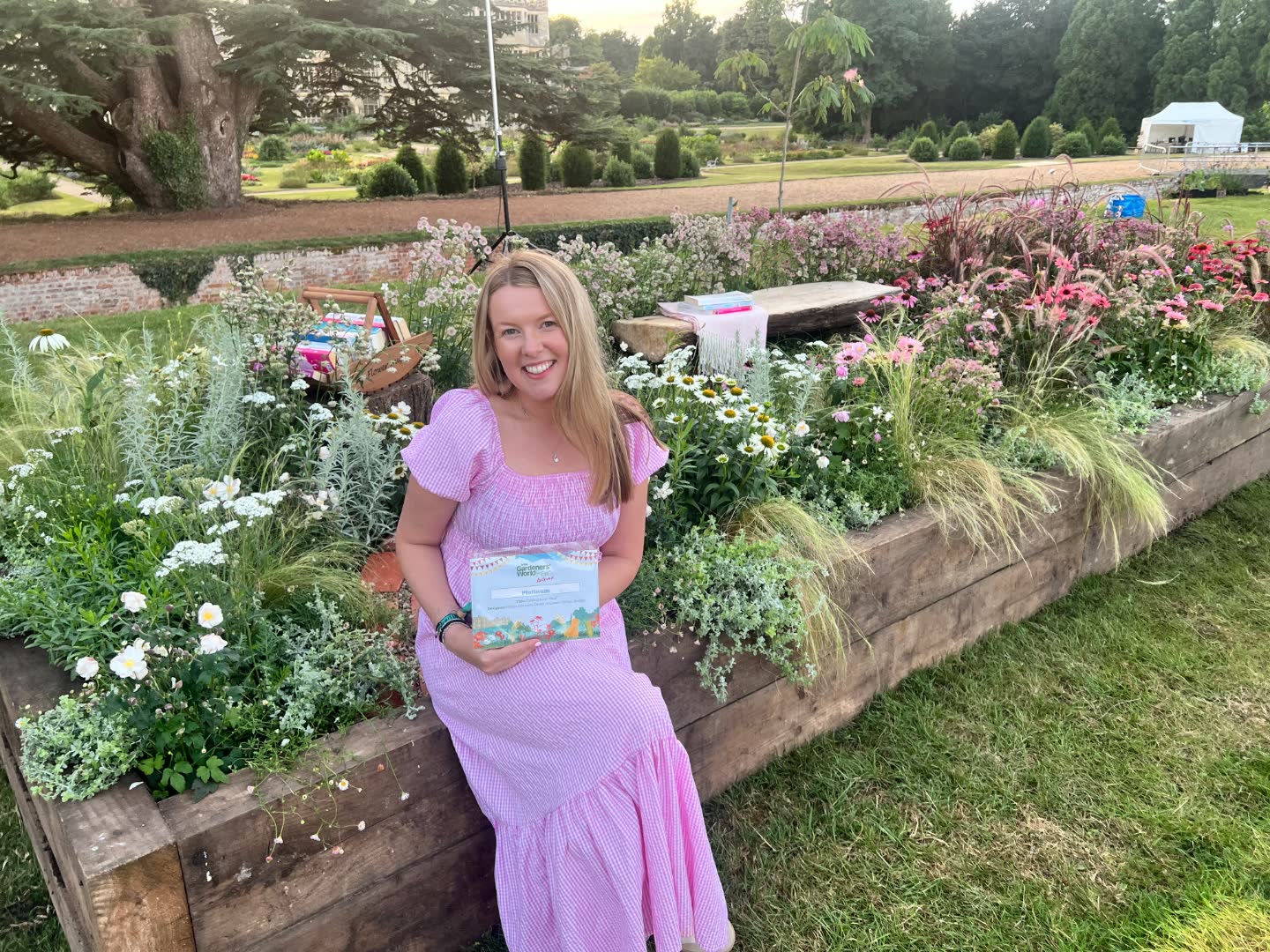 Emma Atkinson in a pink dress, seated by her Platinum-winning Finding Your Pink garden at BBC Gardeners' World Live, Audley End.